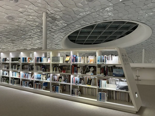 Organized bookshelves within a modern knowledge space, contemporary interior design with soft lighting, innovative architectural ceiling, an educational and cultural environment inside a modern building, King Abdulaziz Center for World Culture (Ithra) in Dhahran.