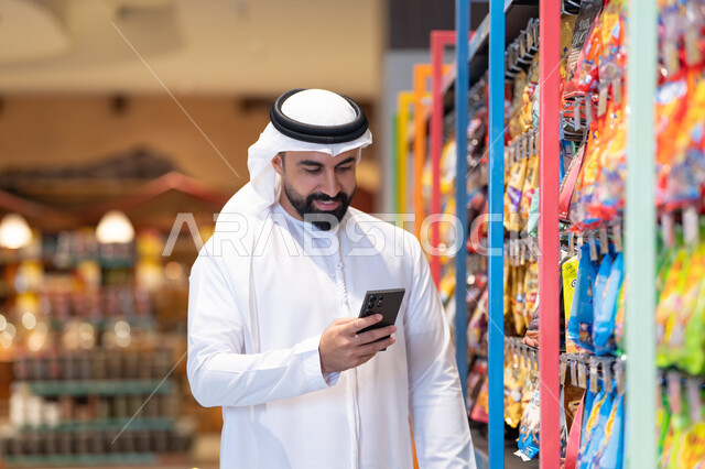 رجل إماراتي يستخدم الهاتف الذكي في السوبر ماركت