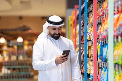 رجل إماراتي يستخدم الهاتف الذكي في السوبر ماركت
