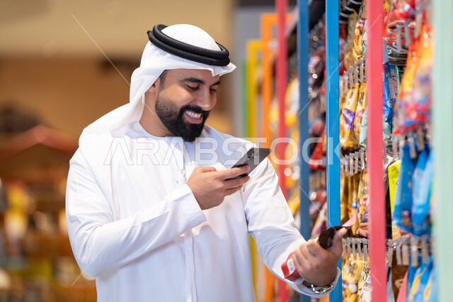 رجل إماراتي يتسوق باستخدام الهاتف الذكي في السوبر ماركت