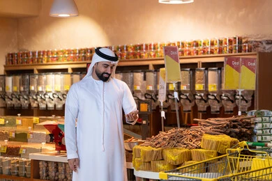 Emirati Man Using Smartphone in Supermarket Spice Aisle