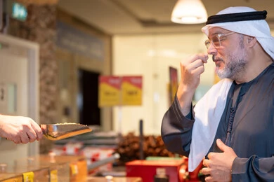 Emirati Man in Traditional Attire Sampling Food at Market