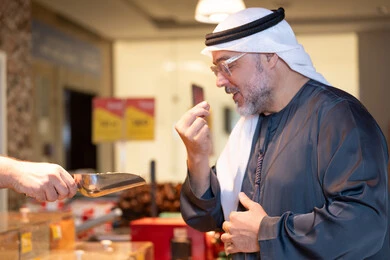 رجل إماراتي يتذوق عينة طعام في سوق تجاري