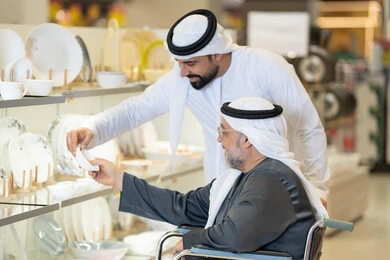 رجل إماراتي يساعد مسناً على كرسي متحرك أثناء التسوق