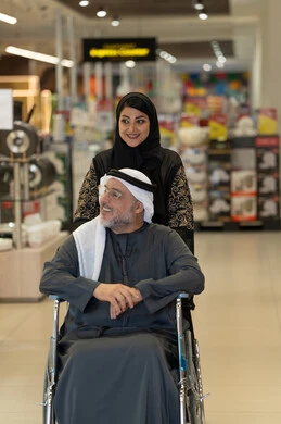 امرأة إماراتية تدفع رجلاً مسناً على كرسي متحرك في المول