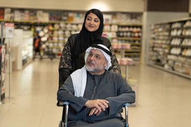 Emirati Woman Helping Elderly Man in Wheelchair Shopping