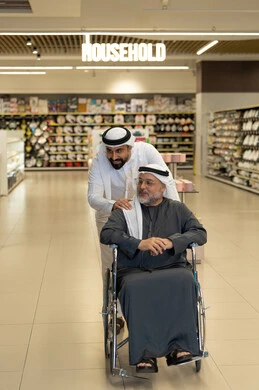رجل إماراتي يدفع مسناً على كرسي متحرك في السوبر ماركت