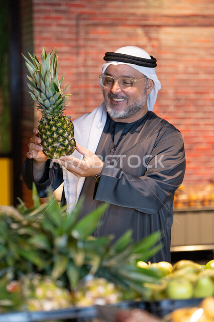 رجل إماراتي في السوبر ماركت يمسك أناناس طازج