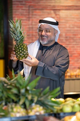 رجل إماراتي في السوبر ماركت يمسك أناناس طازج