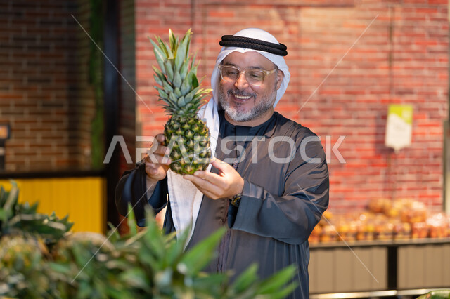رجل إماراتي يتسوق الأناناس الطازج في السوبر ماركت