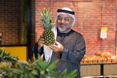 رجل إماراتي يتسوق الأناناس الطازج في السوبر ماركت
