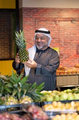 رجل إماراتي يتسوق لشراء الأناناس الطازج من السوبر ماركت
