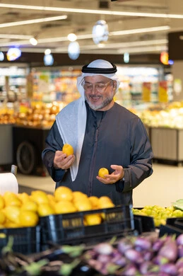 رجل إماراتي يتسوق ويختار الليمون في السوبر ماركت