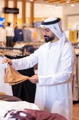 رجل عربي بالكندورة يتسوق في متجر ملابس