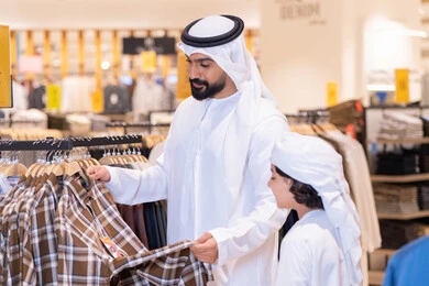 رجل إماراتي وطفل يتسوقان الملابس في المتجر