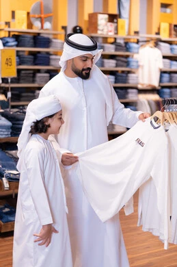رجل إماراتي وطفل يتسوقان الملابس في متجر حديث