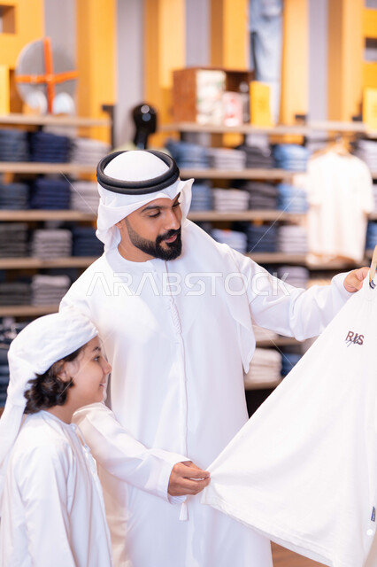أب وابنه بزي إماراتي يتسوقان الملابس في متجر حديث