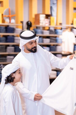 أب وابنه بزي إماراتي يتسوقان الملابس في متجر حديث أب وابنه بزي إماراتي يتسوقان الملابس في متجر حديث