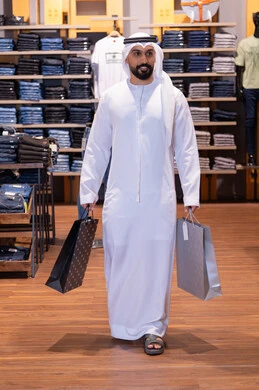 رجل إماراتي يحمل أكياس تسوق داخل متجر ملابس
