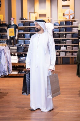 رجل إماراتي ينظر جانباً يحمل أكياس تسوق داخل متجر ملابس