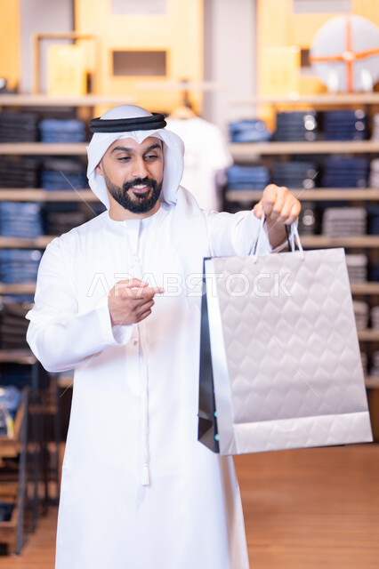رجل إماراتي يحمل حقيبة تسوق فضية في متجر ملابس حديث