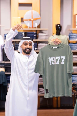 Emirati Man Holding T-Shirt in Retail Clothing Store