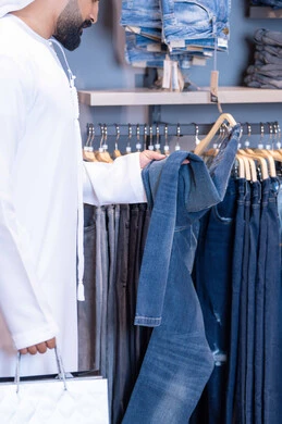 رجل عربي يتسوق لشراء بنطال جينز في متجر ملابس