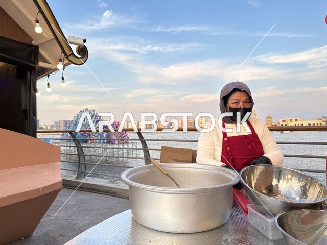 An Asian woman is preparing food in the Global City in January 2026 on the shores of the Arabian Gulf and Lake Sehat in the Eastern Province of Dammam. She is familiar with the different cultures of the country, which is a tourist and entertainment attraction, stimulating tourism and economic activity, and a place to spend enjoyable time with family.