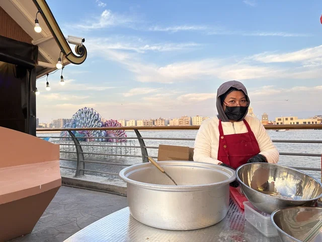 سيدة اسيوية تقوم بتحضير الطعام في المدينة العالمية يناير 2026 على ضفاف الخليج العربي وبحيرة سيهات في المنطقة الشرقية الدمام، تعرف ثقافة البلاد المختلفة، معلم جذب سياحي وترفيهي، تنشيط الحركة السياحية والاقتصادية، مكان لقضاء وقت ممتع مع العائلة