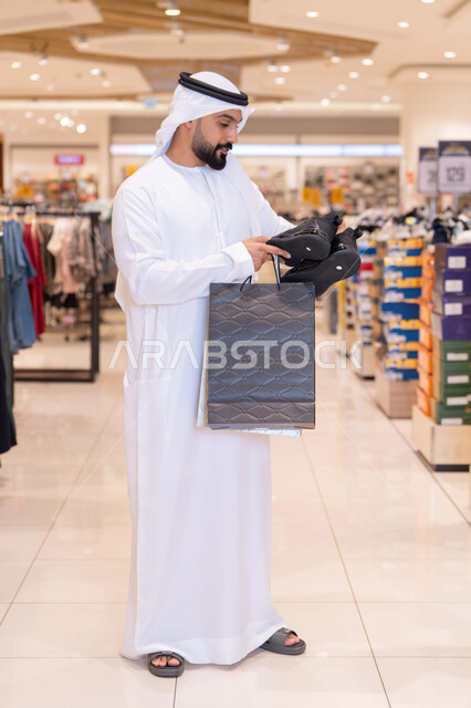 رجل إماراتي يحمل حقائب تسوق في مركز تجاري حديث