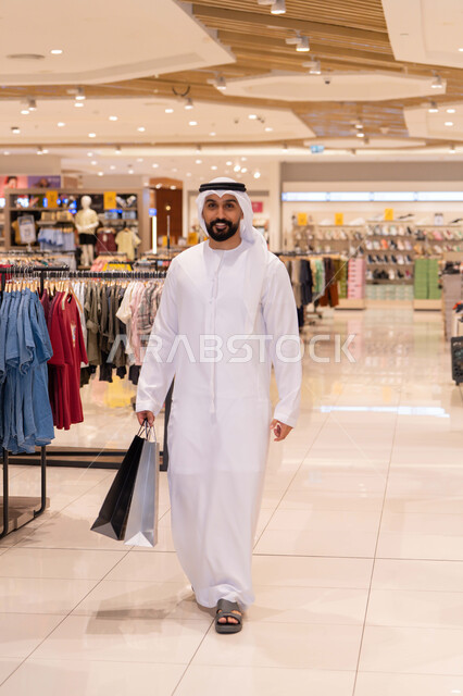 رجل إماراتي يحمل حقائب تسوق في مول حديث