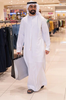 رجل إماراتي يسير في مول تجاري مع حقائب تسوق