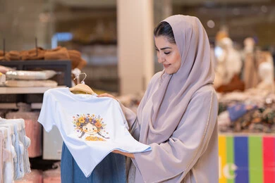 امرأة عربية تتسوق ملابس أطفال في متجر تجزئة