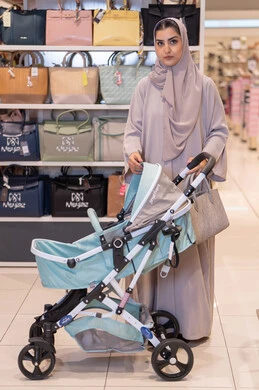 امرأة عربية مع عربة أطفال في متجر حقائب