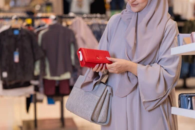 امرأة عربية تتفحص محفظة حمراء في متجر ملابس