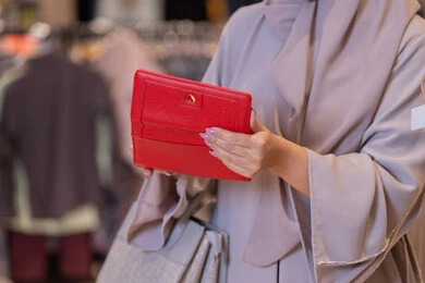 امرأة عربية تحمل محفظة حمراء في متجر ملابس