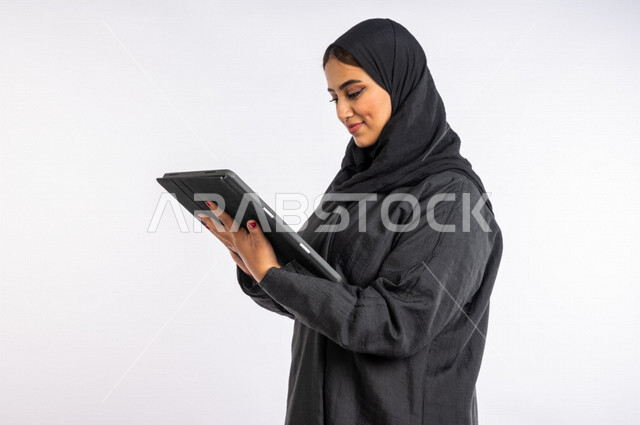 Portrait of a Saudi Arabian Gulf woman, using a tablet device to accomplish tasks, remote work, entertainment, work session, professions and jobs, the concept of technology and the use of modern technical devices, e-marketing, surfing the Internet, using 