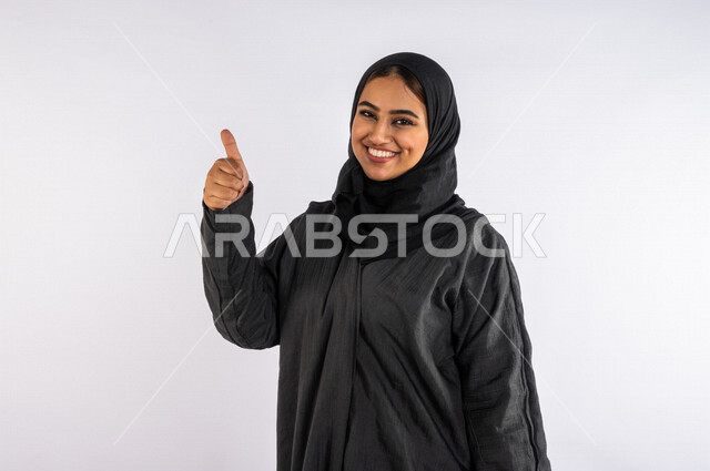 بورتريه لمرأة عربية خليجية سعودية ، مبتمسة تنظر إلى الكاميرا ، تشير بإصبعها الإبهام ، بإيماءات وجه ويدين مختلفة تدل على الإعجاب ، ترتدي العباءة الخليجية ، خلفية بيضاء 