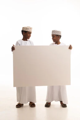 طفلان عمانيان يمسكان بلوحة بيضاء فارغة بخلفية بيضاء
