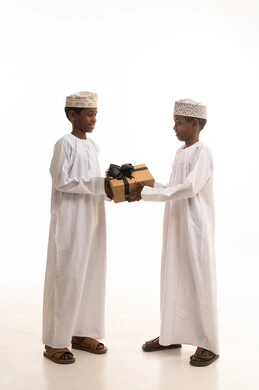 صبية عمانيون بالزي التقليدي يتبادلون صندوق هدايا