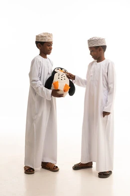 أطفال عمانيون بالزي التقليدي يلعبون بلعبة محشوة