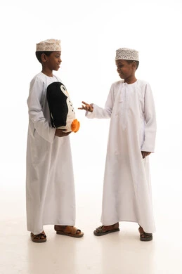 أطفال عمانيون بالزي التقليدي يحملون لعبة بطريق في الاستوديو