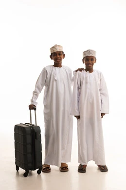 أطفال عمانيون مع حقيبة سفر بخلفية بيضاء