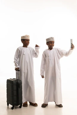 أطفال عمانيون بالزي التقليدي يلتقطون سيلفي مع حقيبة سفر