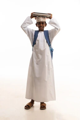 طالب مدرسي عماني يحمل كتباً وحقيبة بزي تقليدي