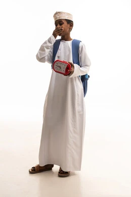 طفل عماني يتثاءب مع ساعة منبه وحقيبة مدرسية