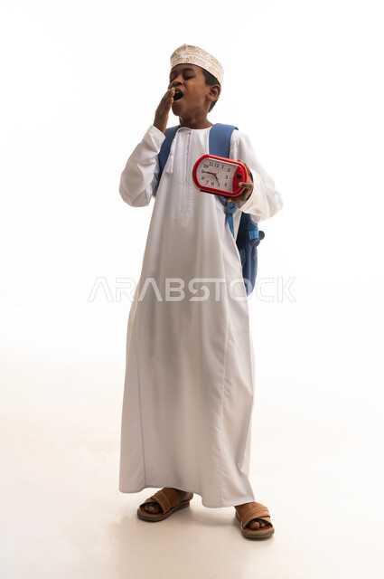 طالب عماني يتثاءب مع ساعة منبه وحقيبة