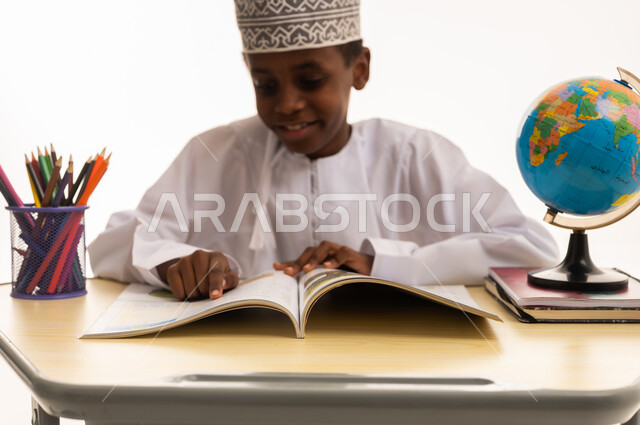 طفل عماني يقرأ كتاب على مكتب مع كرة أرضية