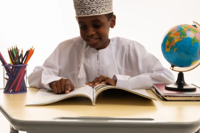 طفل عماني يقرأ كتاب على مكتب مع كرة أرضية طفل عماني يقرأ كتاب على مكتب مع كرة أرضية