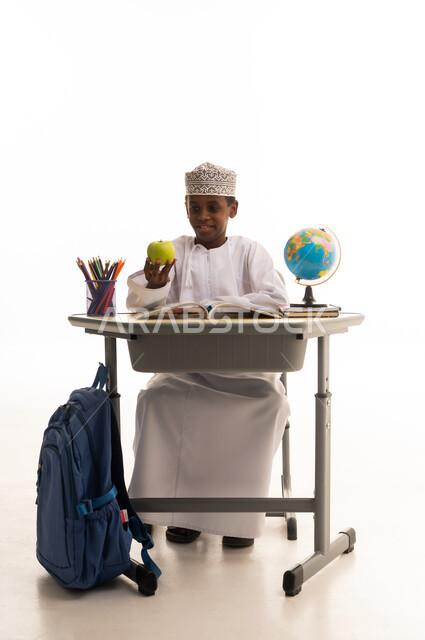 طالب عماني جالس على مقعد دراسي مع تفاحة خضراء